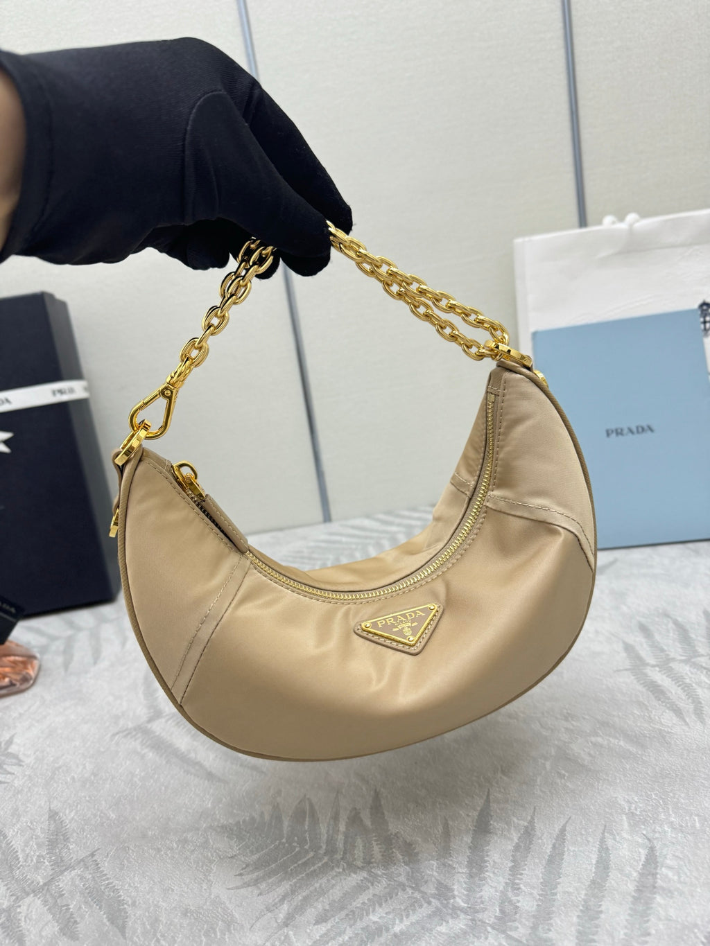 Beige shoulder bag with gold chain strap and triangular logo on the front