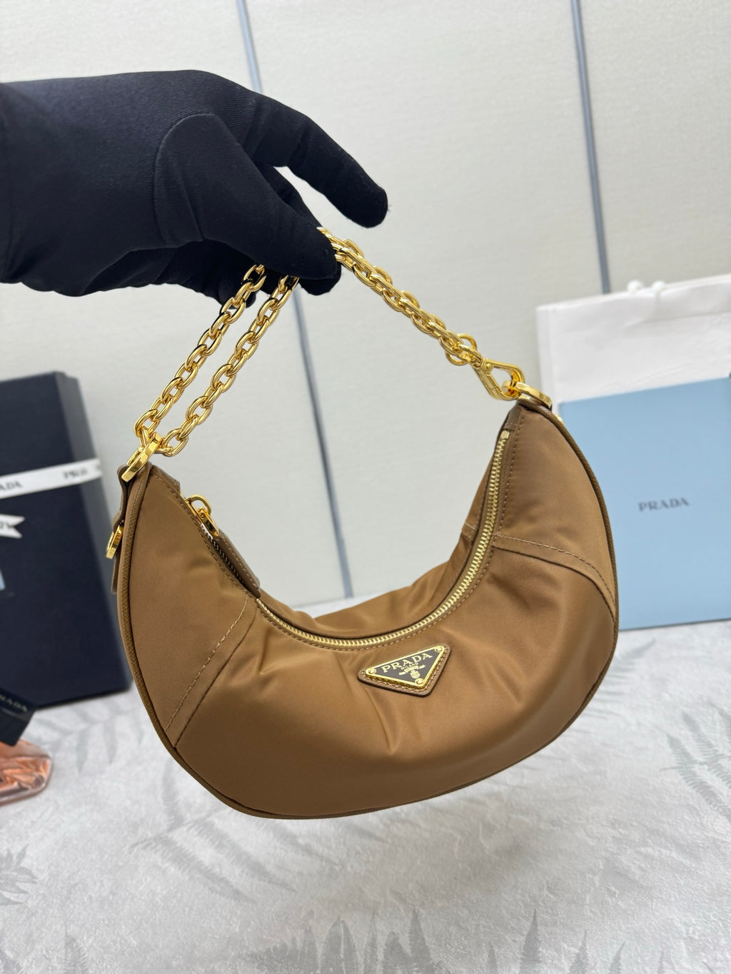 Prada tan leather hobo bag held by gold chain strap, with front crest logo badge.