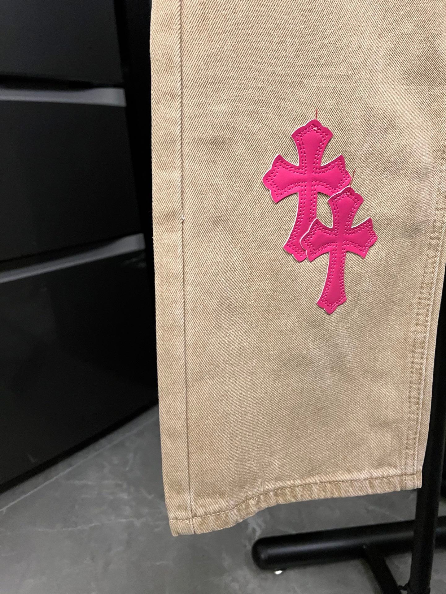 Beige denim pants with small pink cross embroidery on leg