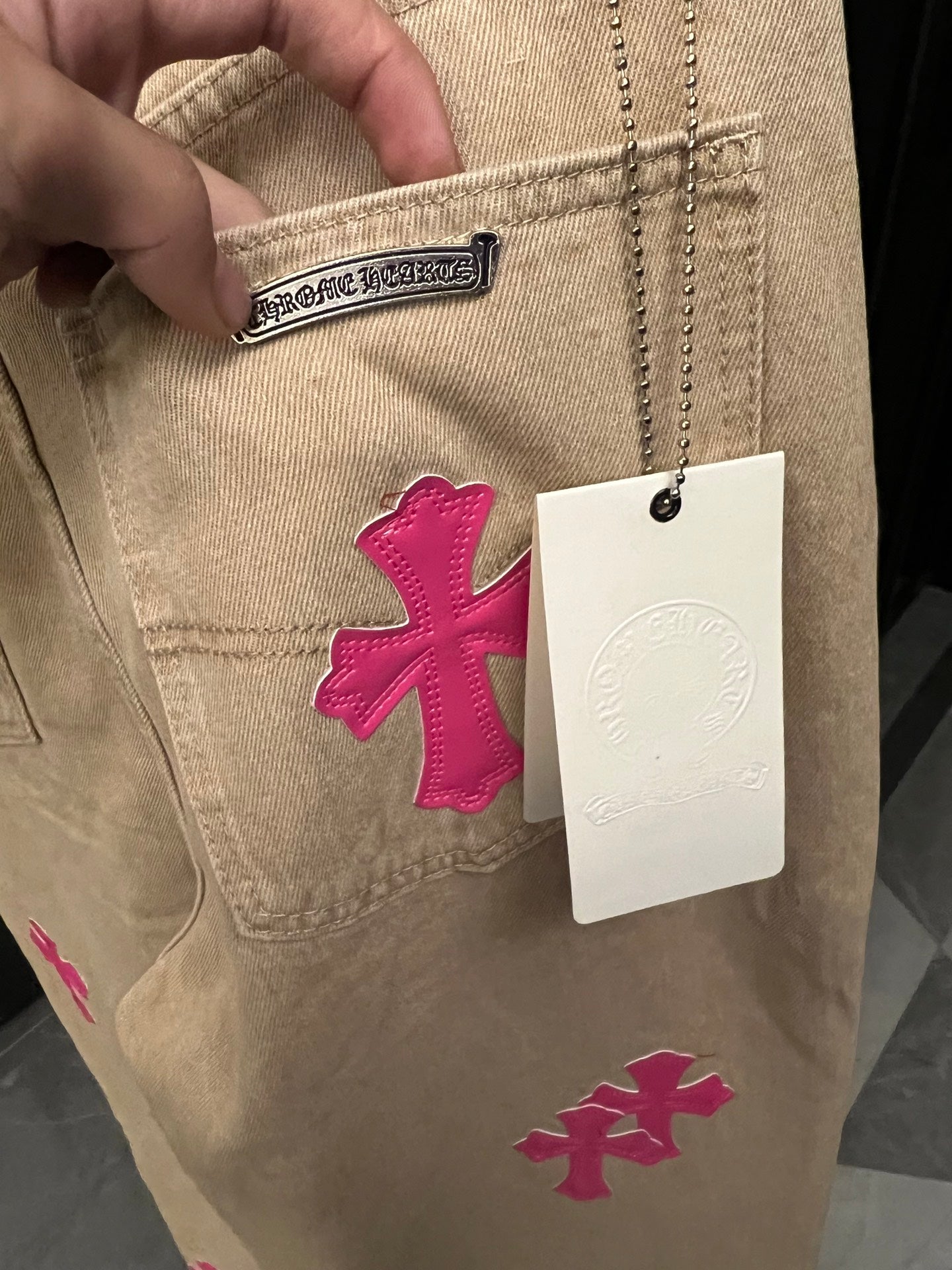 Beige denim pants with pink cross embroidery and attached size tag