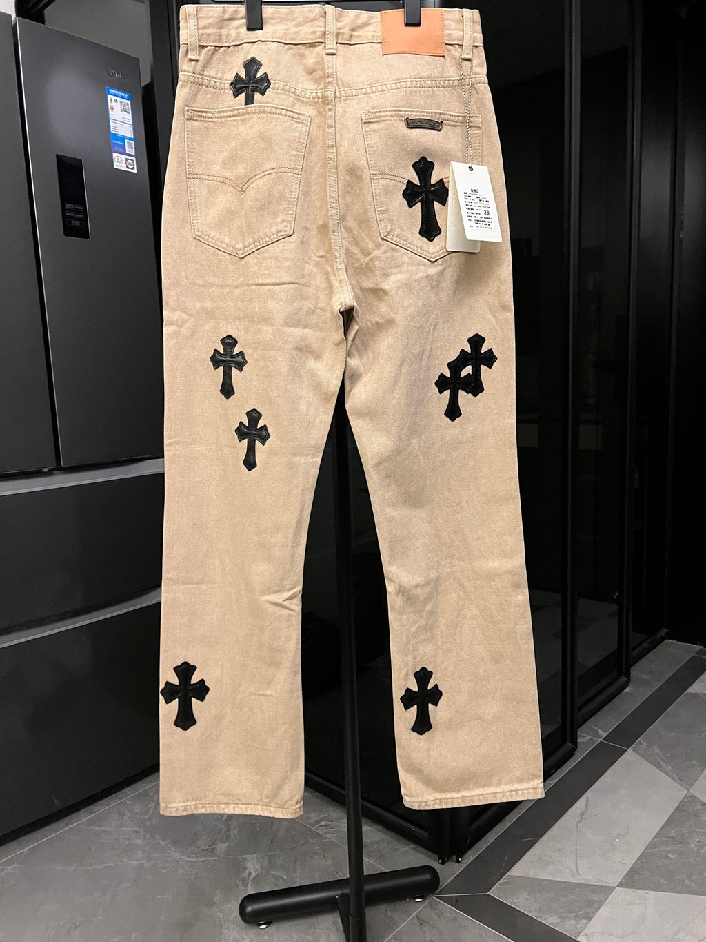 Beige denim pants with black cross patches on front legs and back pockets