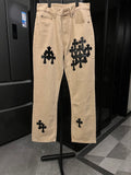 Beige denim pants with black cross-style patches and belt loops