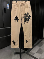 Beige denim pants with black cross-style patches and belt loops