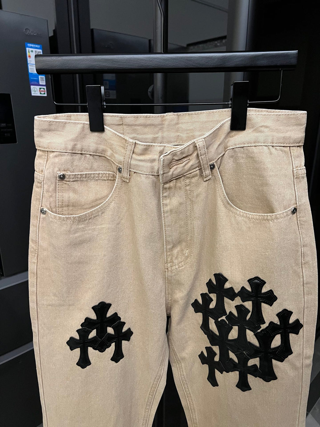 Beige denim pants with black cross patches at thighs and front pockets