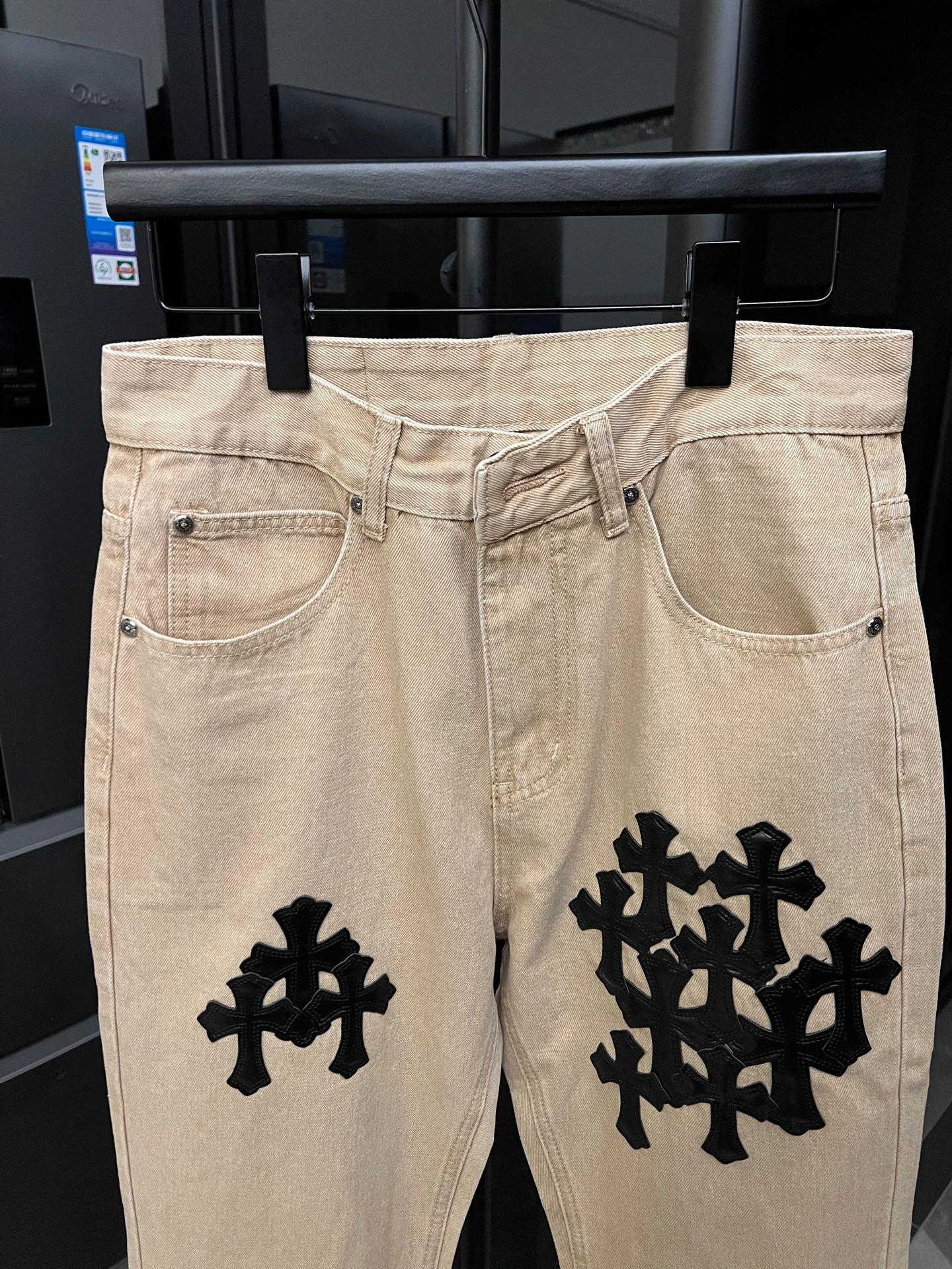 Beige denim pants with black cross patches at thighs and front pockets