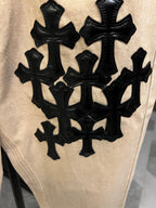 Beige denim pants with large black cross patch across thigh area