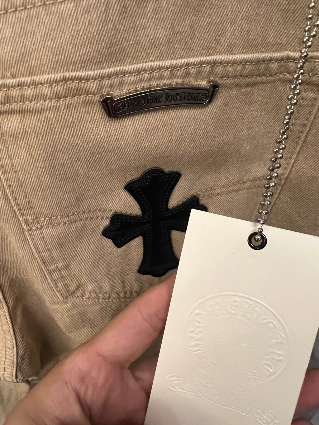 Beige denim pants with black cross patch and small logo label