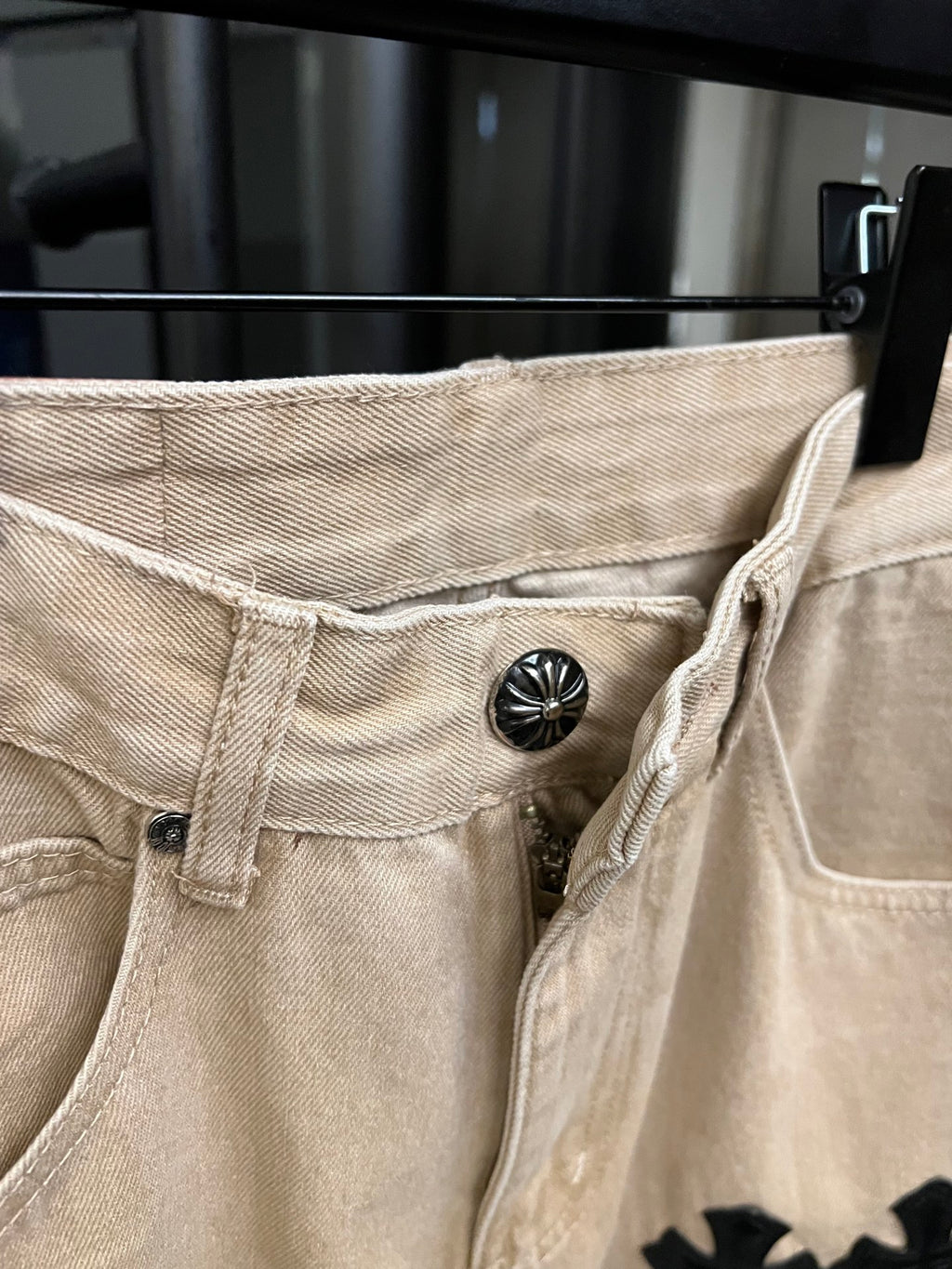 Beige denim pants with button closure and black cross patch on side
