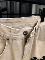 Beige denim pants with button closure and black cross patch on side