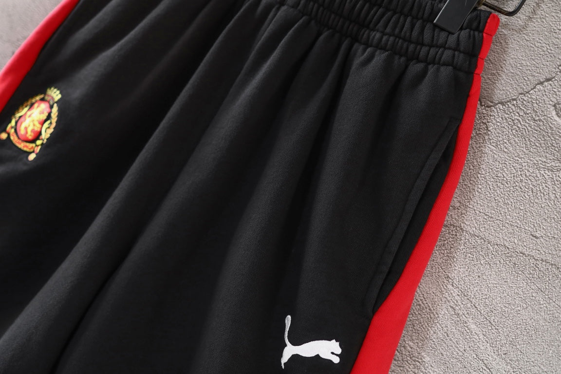 Black pants with puma logo print, pleated front, and red side panel