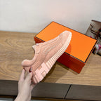 Hermes light pink lace-up sneaker held in hand over orange shoebox