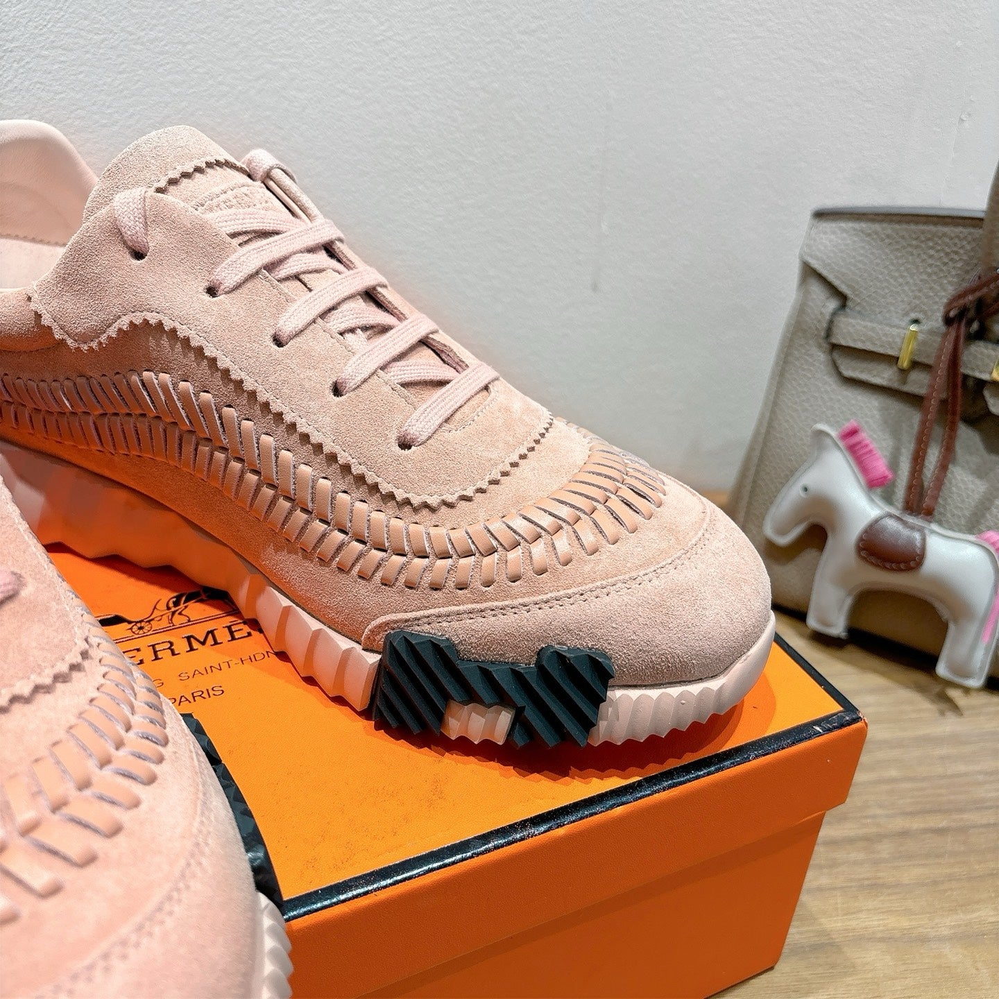 Hermes light pink suede sneaker close-up with lace-up eyelets and ridged side panel
