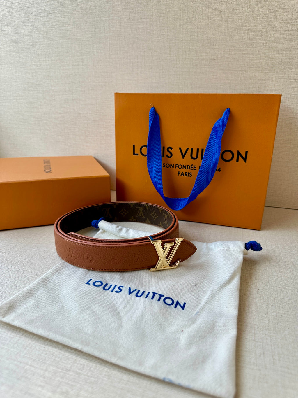 Louis Vuitton belt on a white pouch: brown leather strap and LV silver-tone buckle.