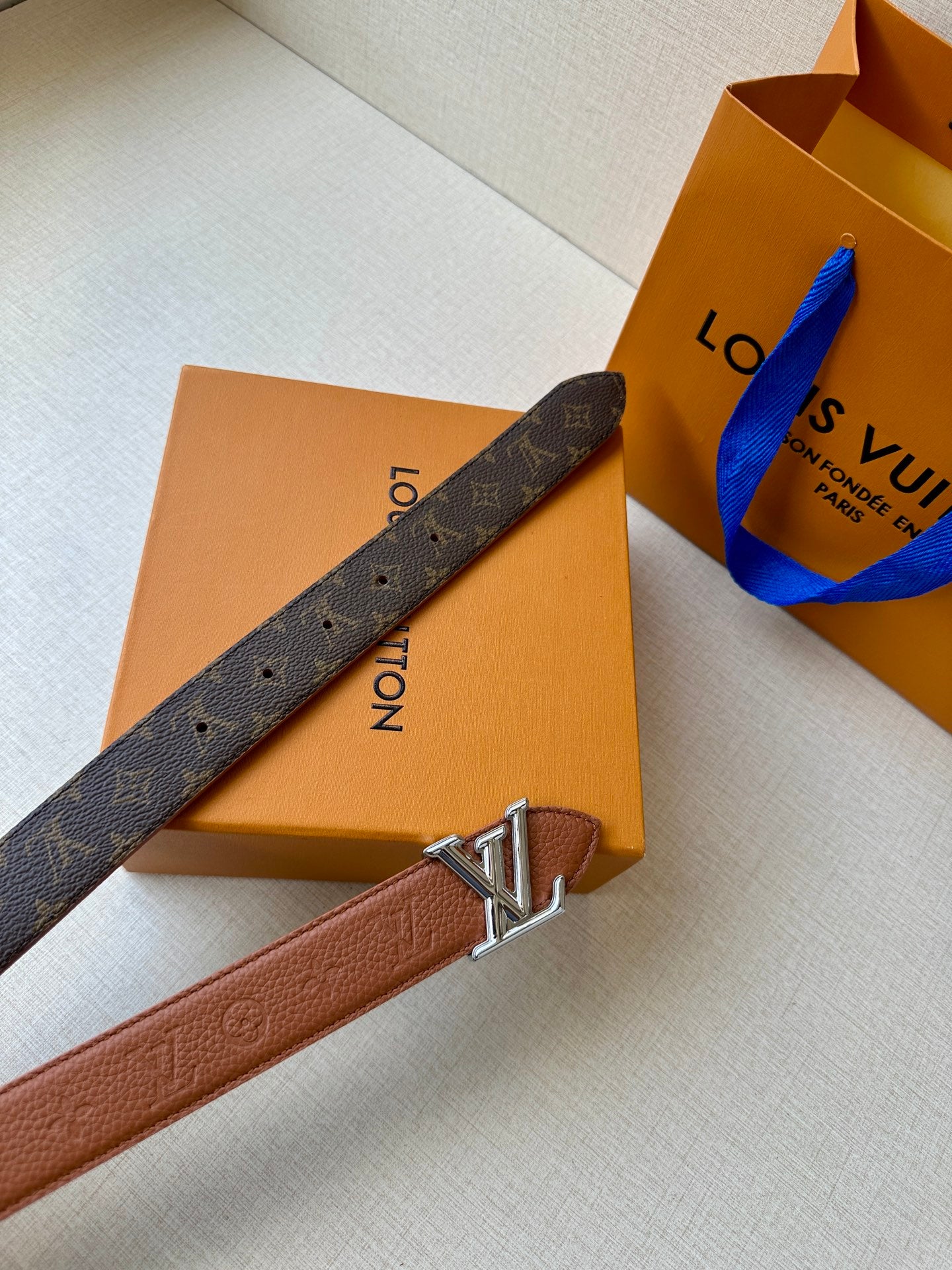 Louis Vuitton belt with brown leather strap and LV silver-tone buckle, flat view.