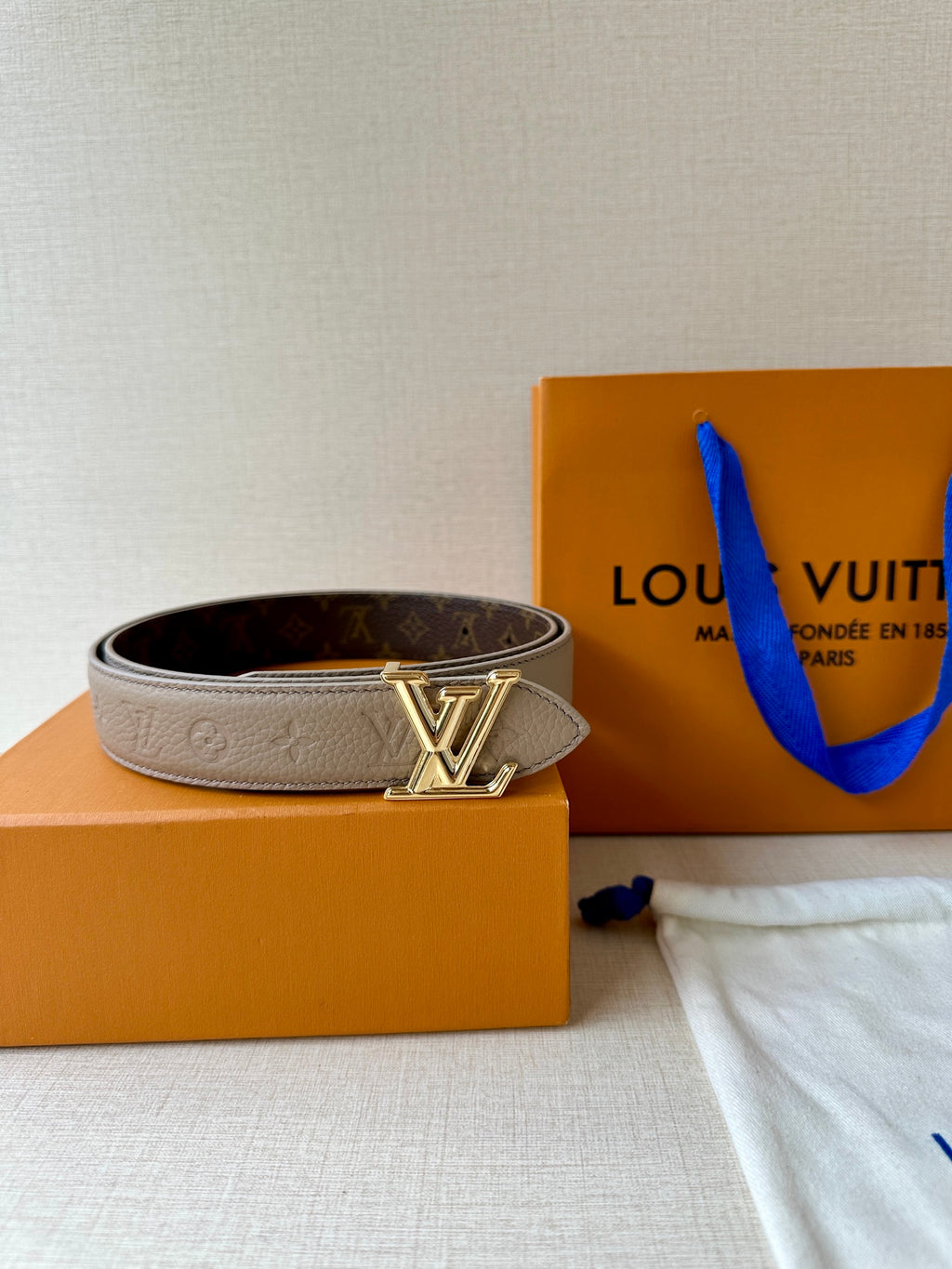 Beige monogram belt with gold-tone LV buckle across the strap