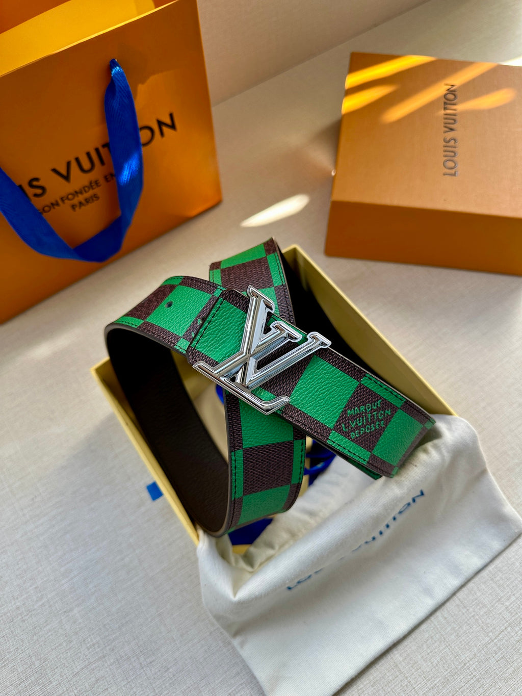Louis Vuitton belt with green check pattern and silver LV buckle resting on pouch