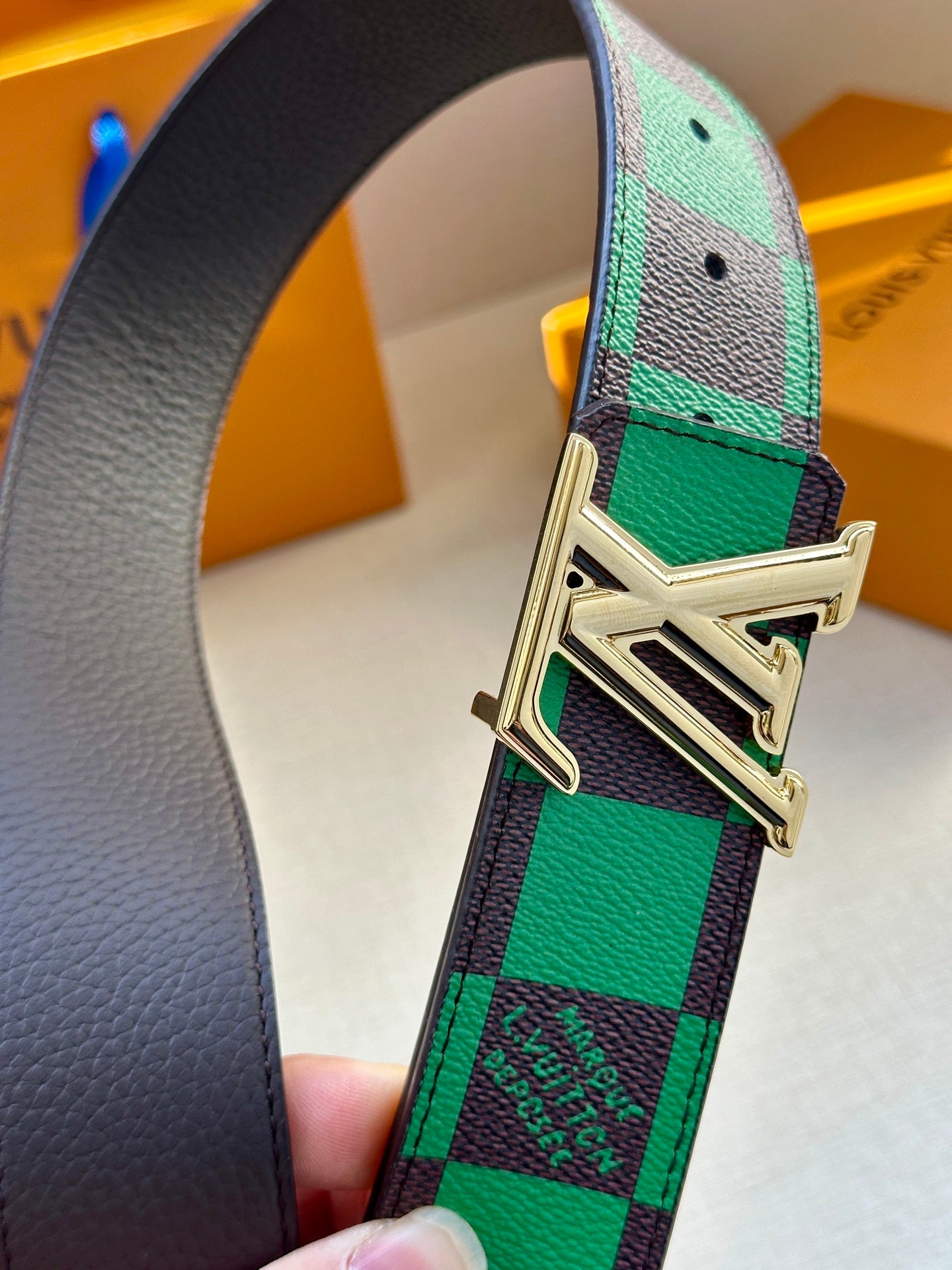 Louis Vuitton belt buckle close-up on green-and-black check strap