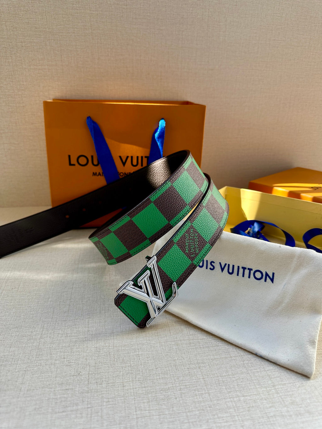 Louis Vuitton belt with green check strap and silver LV buckle on white pouch