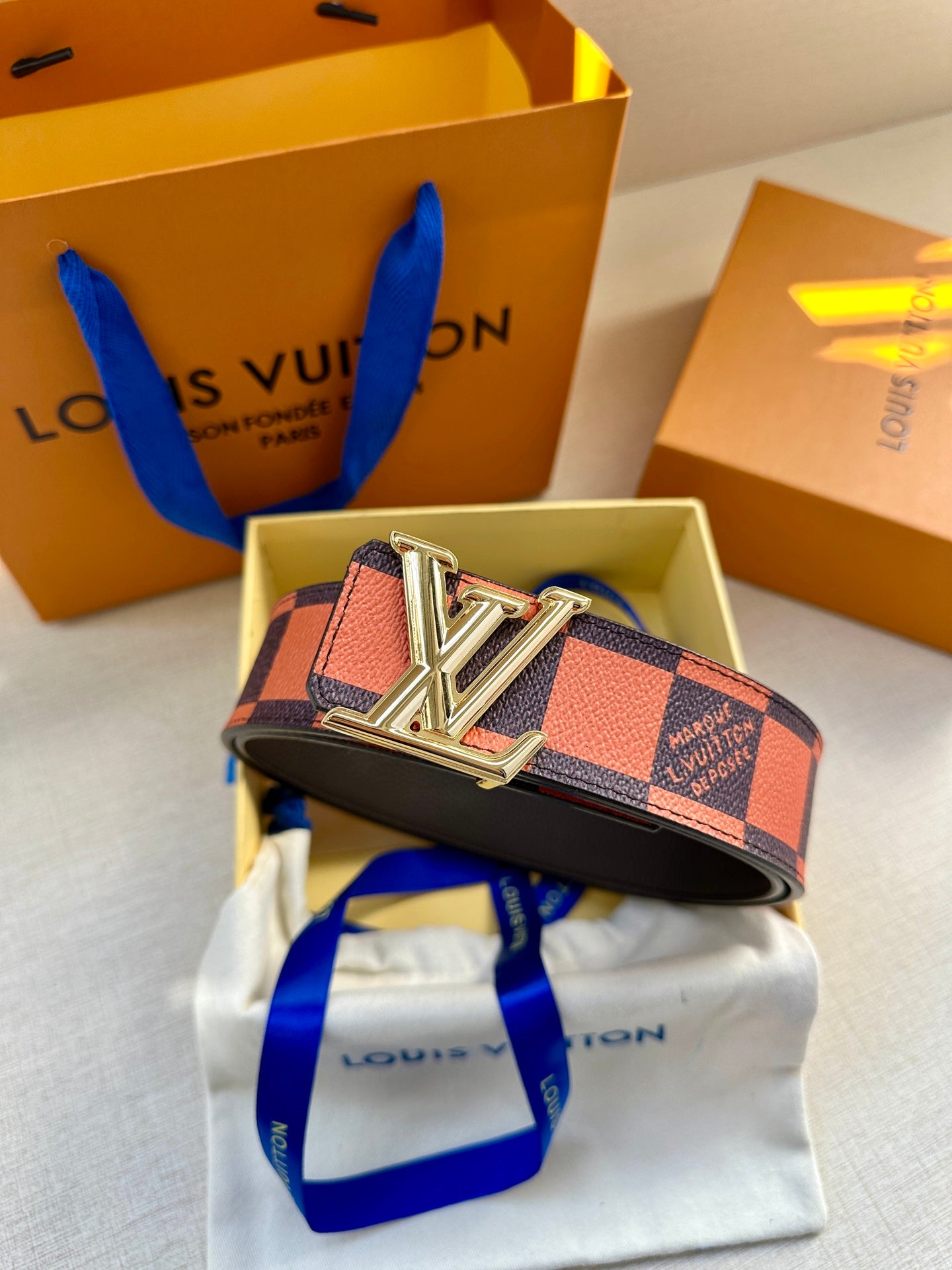 Orange and navy checker belt with silver buckle resting on white pouch