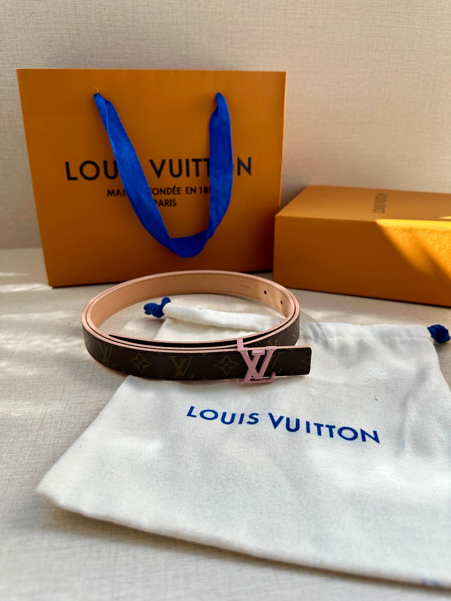 Louis Vuitton belt with dark monogram print, tan trim, and pink LV buckle