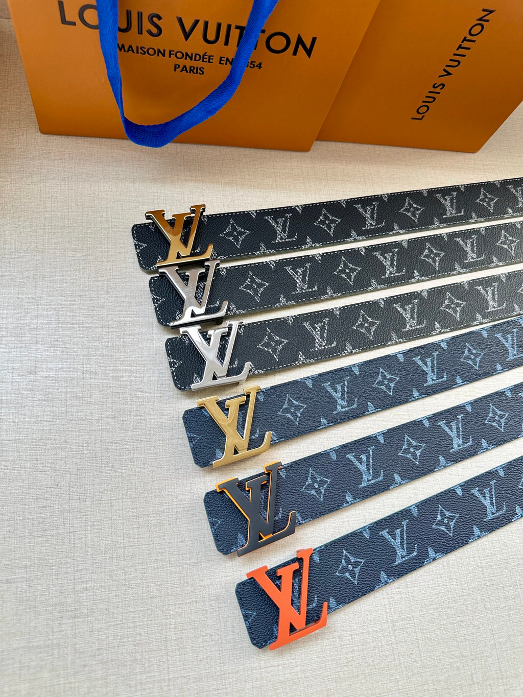 Louis Vuitton belts stacked: navy monogram straps with gold and silver LV buckles
