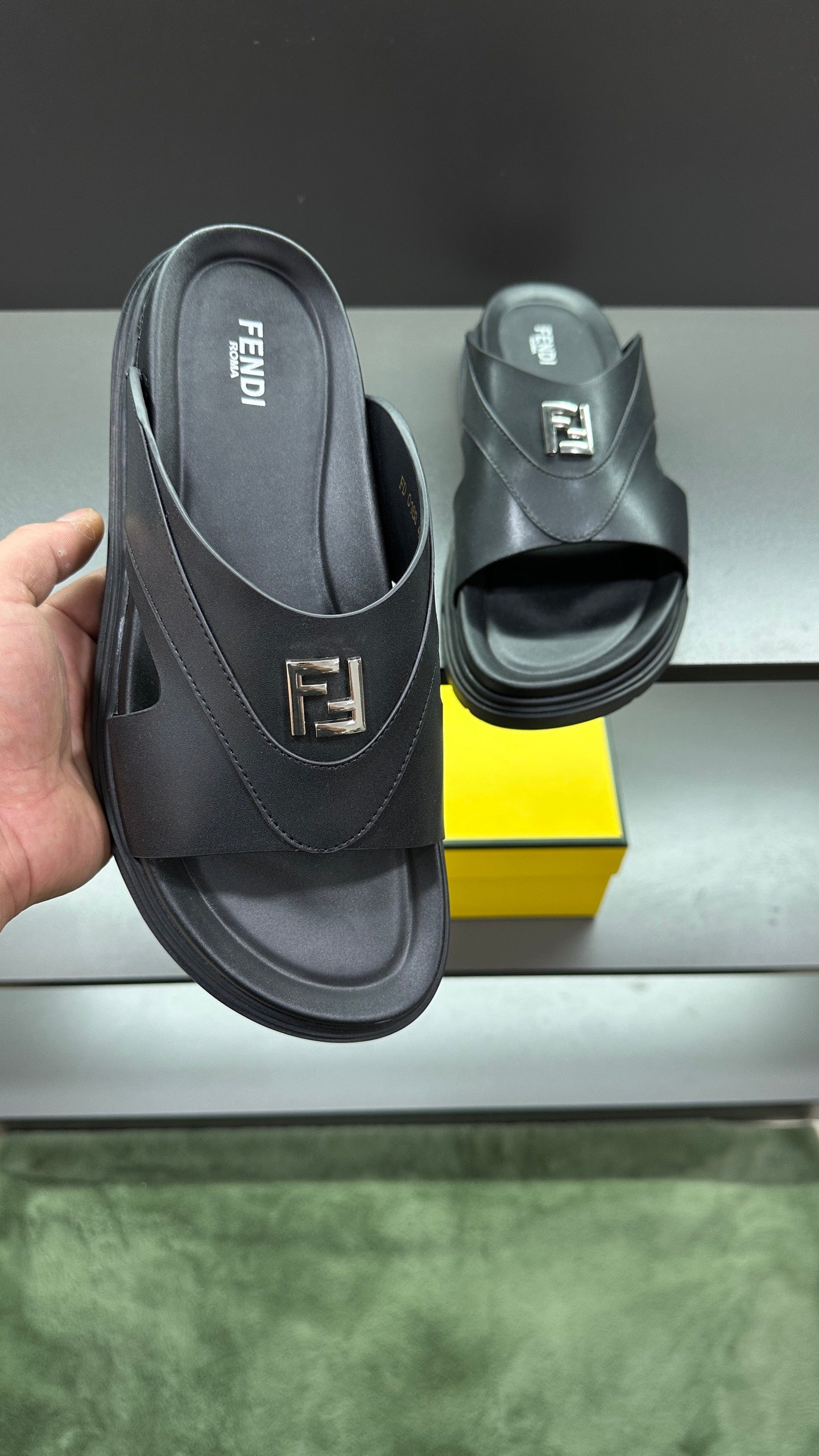 Fendi dark slip-on sandals, logo strap and wide sole, held next to box