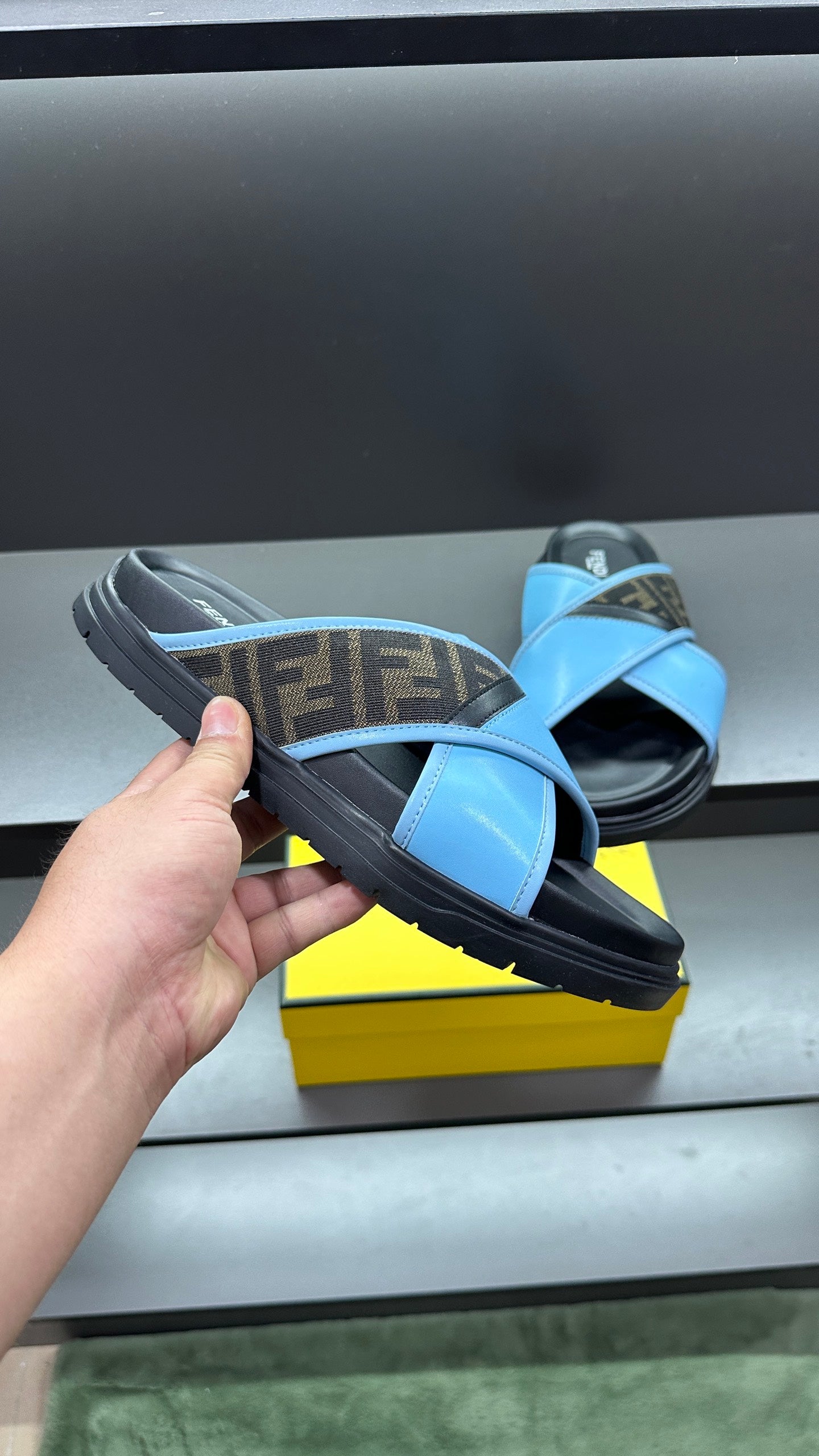 Fendi blue sandals held near box, showing cross straps and cushioned dark sole