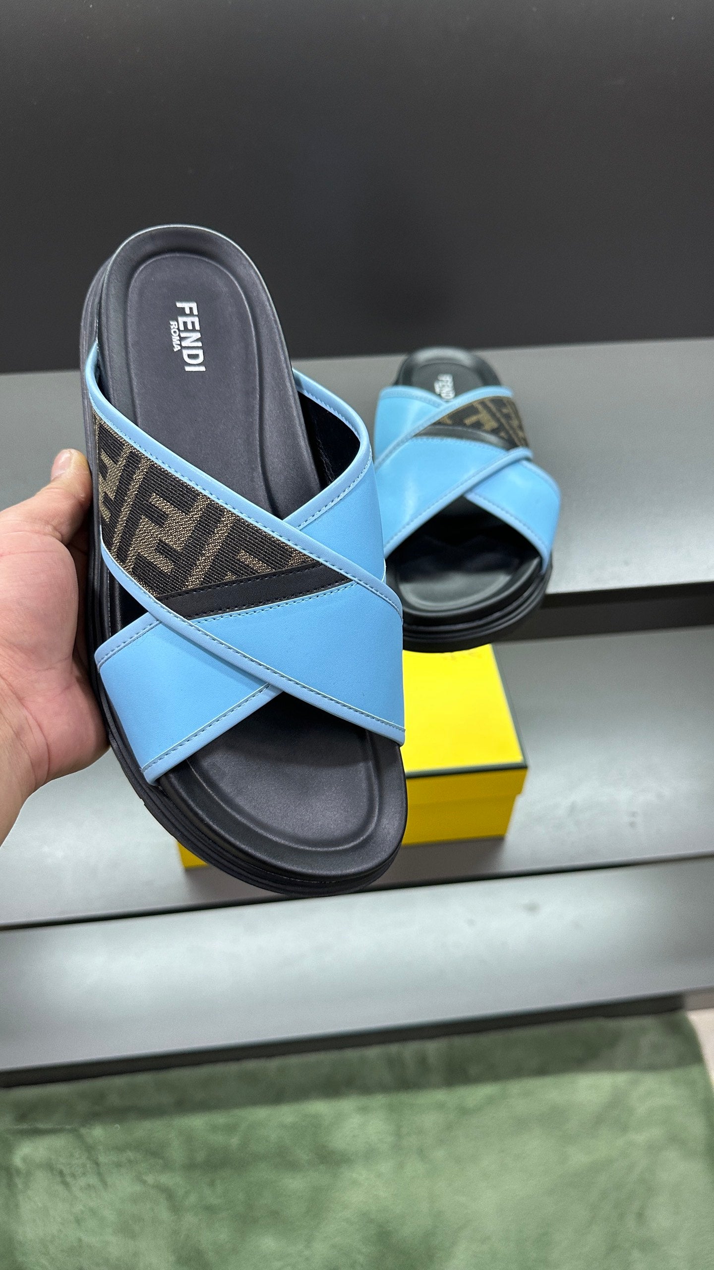 Fendi blue sandals held in hand, showing cross straps and dark rubber footbed