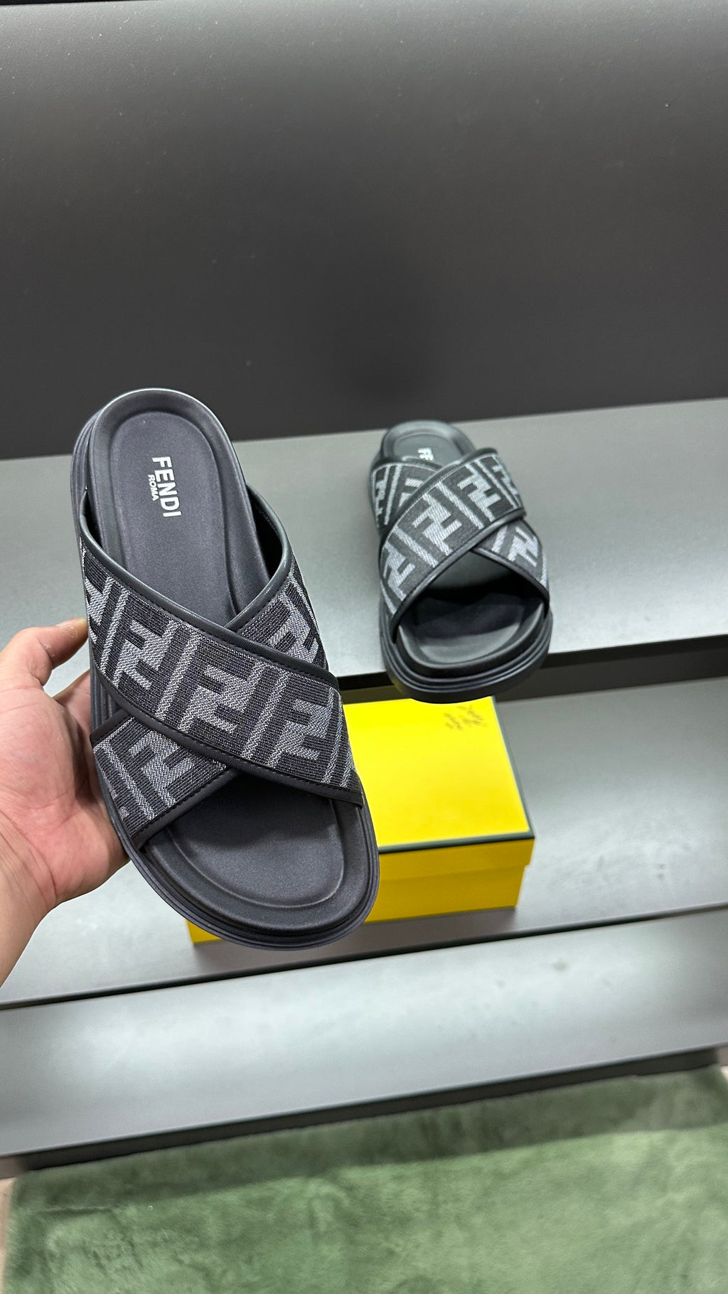 Fendi FF logo slide sandals held in hand, dark gray straps and black footbeds