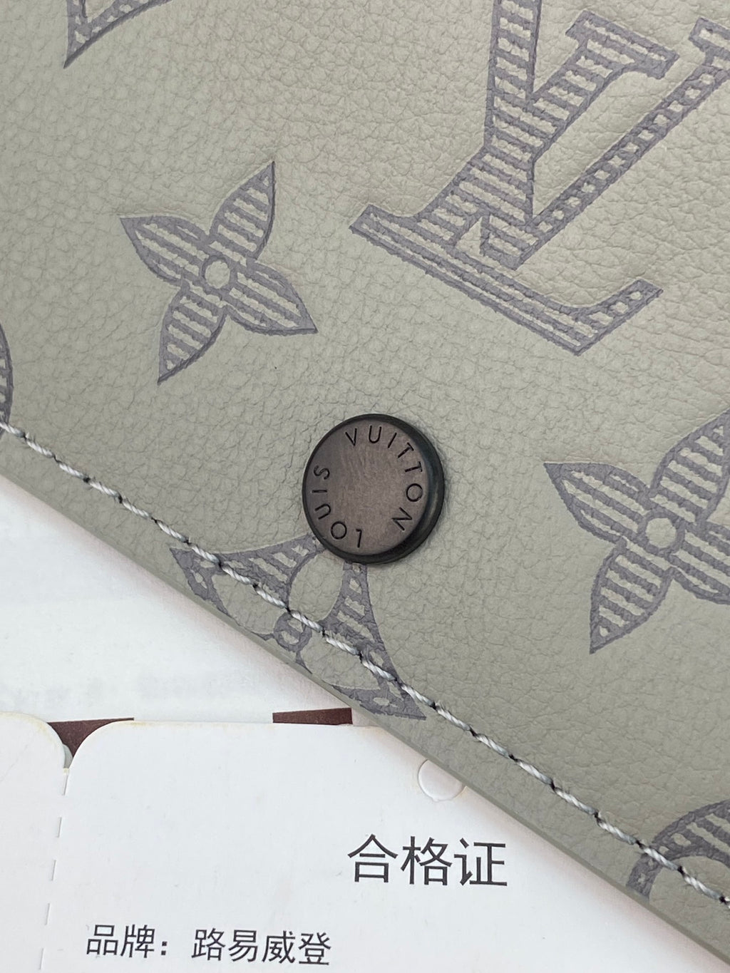 Small bag close-up of snap button and monogram pattern with stitched edge.