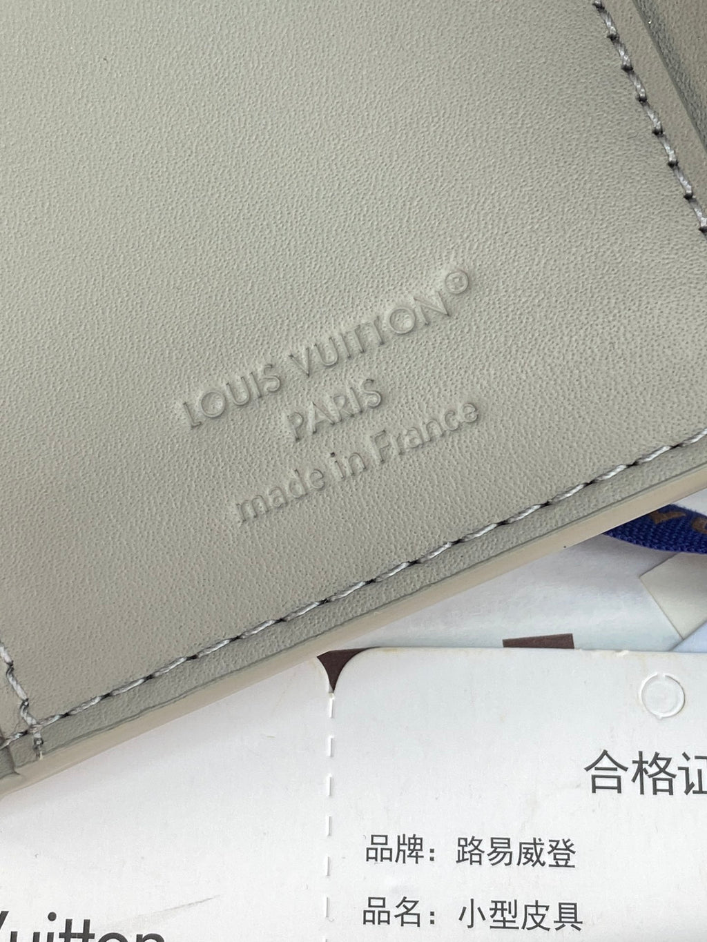 Small bag close-up of embossed "Louis Vuitton" logo on light gray leather.