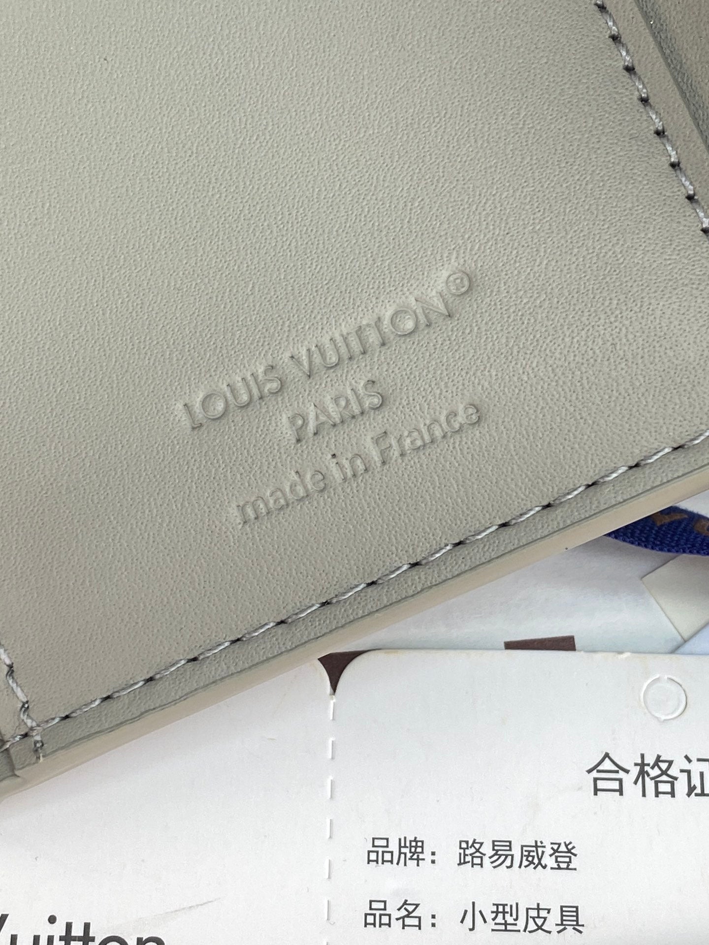 Small bag close-up of embossed "Louis Vuitton" logo on light gray leather.
