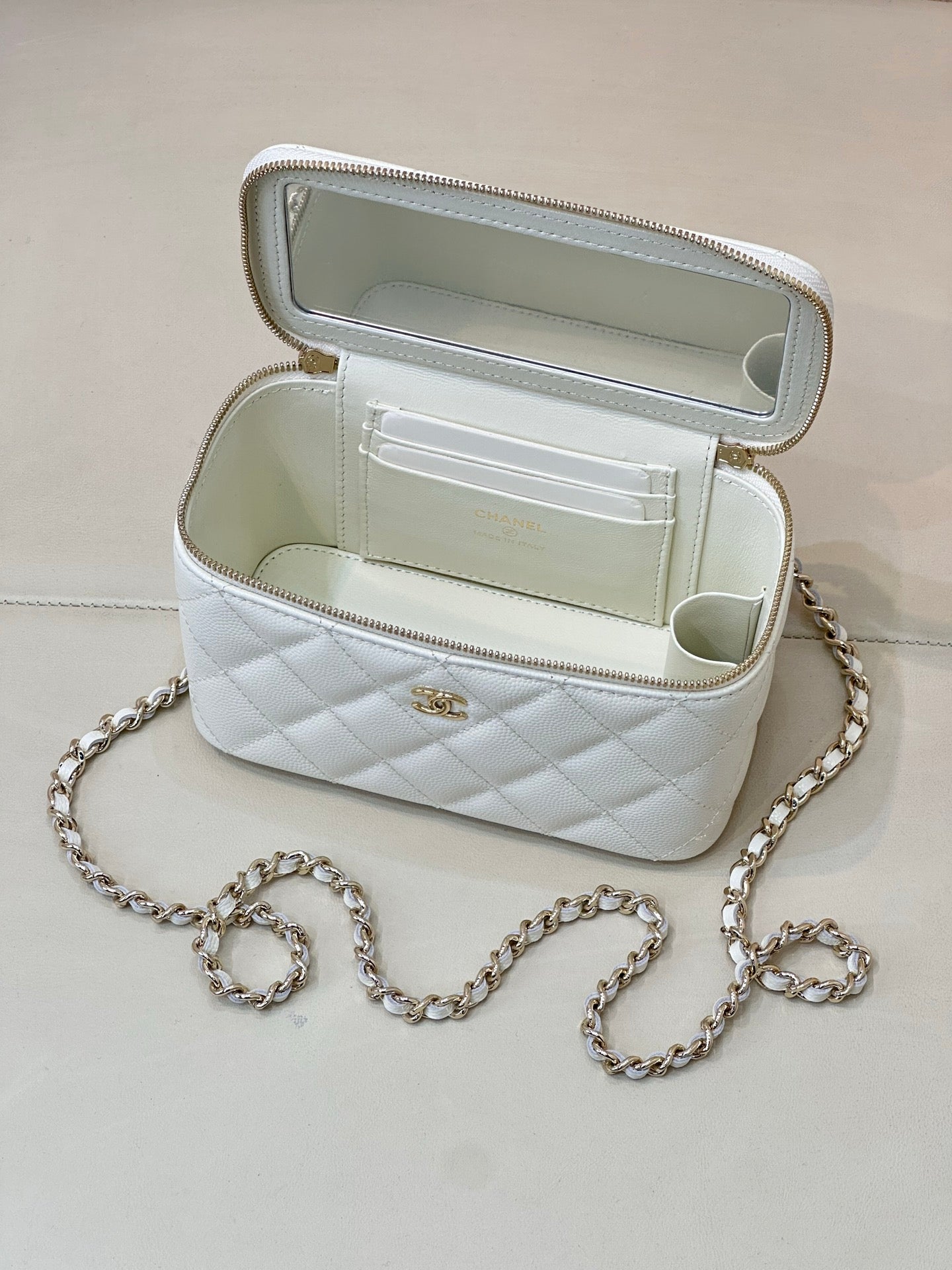 Chanel white quilted bag open, zip top with CC logo, chain strap visible.