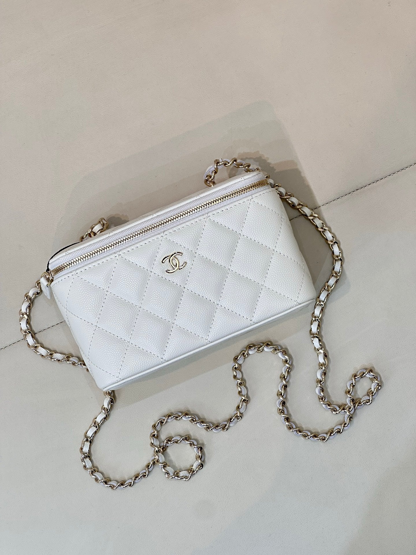 Chanel white quilted crossbody bag with chain strap, zip top, CC logo front.