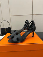 Black leather heeled sandals with cross-over straps, square toe, and thin stiletto heel