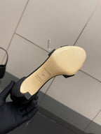 Beige rubber outsole of black heeled sandal with brand text near the heel