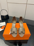 Light gray heeled sandals with open toe, ankle strap, and decorative metal buckle.