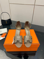Light gray heeled sandals with open toe, ankle strap, and decorative metal buckle.
