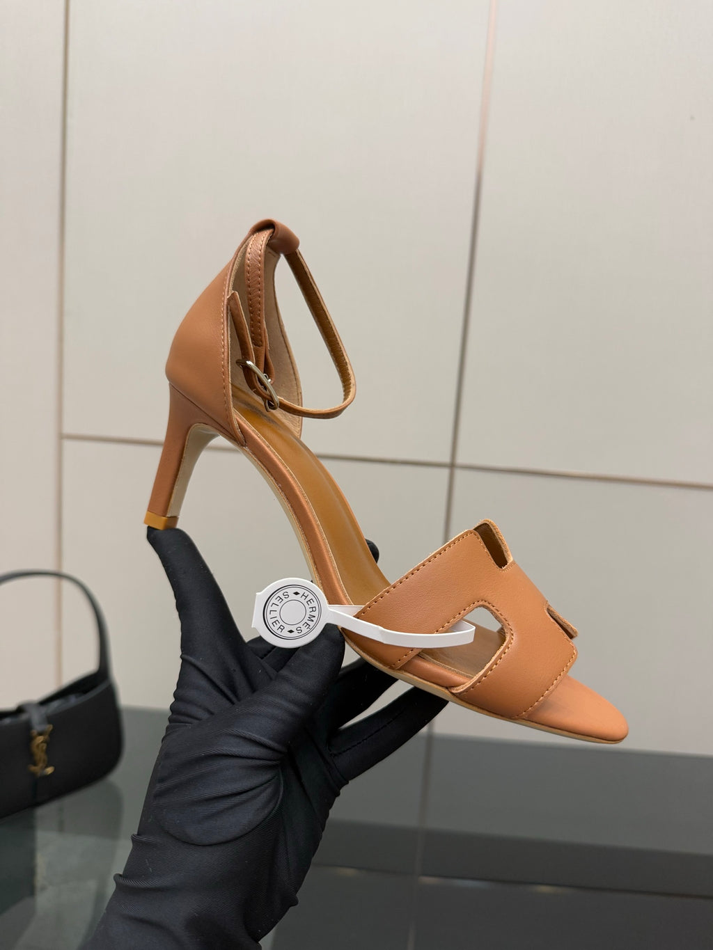 Tan leather heeled sandal held in hand with open toe and H-cutout front