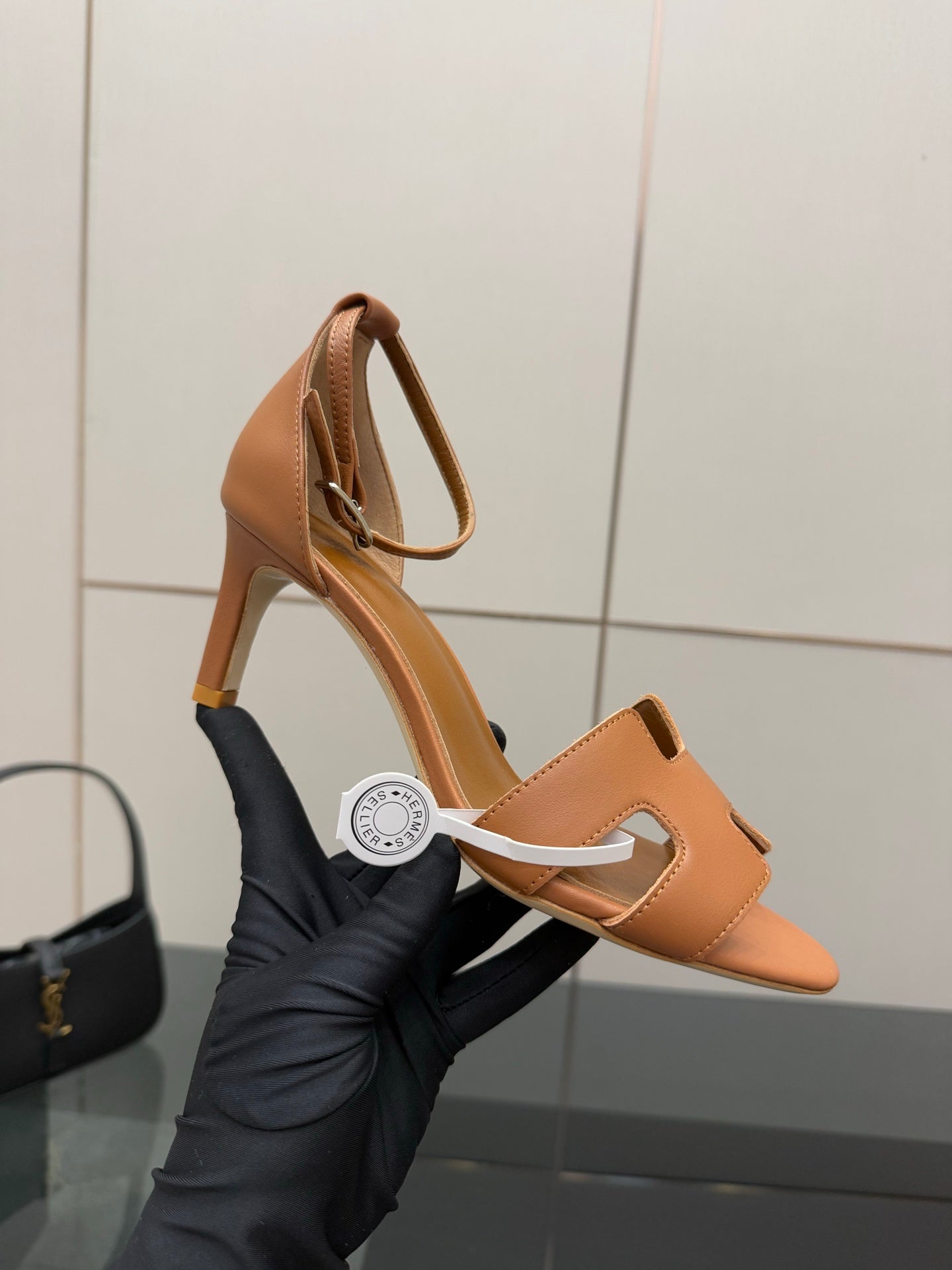 Tan leather heeled sandal held in hand with open toe and H-cutout front