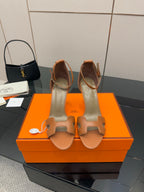 Tan leather heeled sandals with two strap cutouts on an orange presentation box