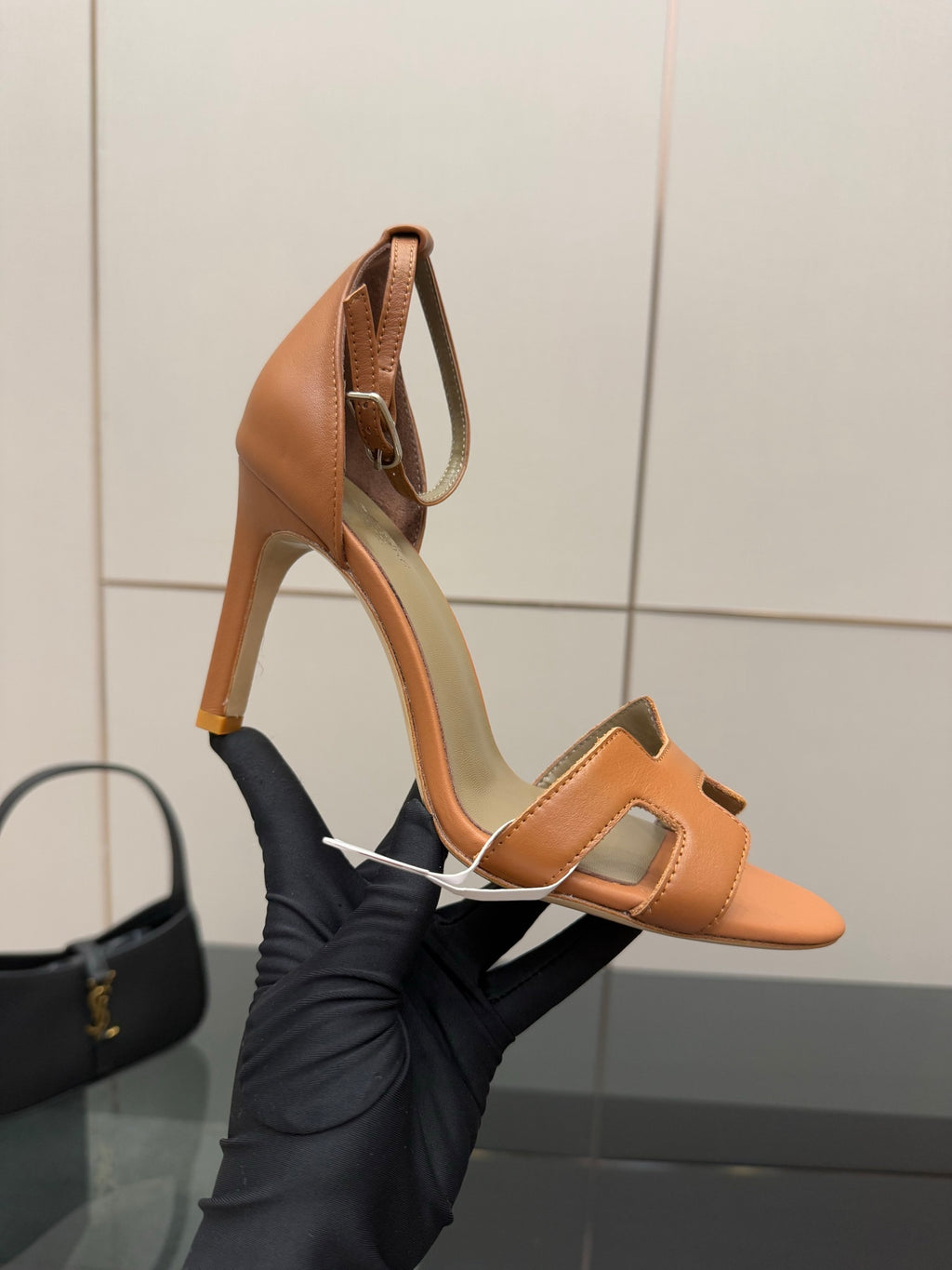 Tan leather heeled sandal held in hand, showing open toe and ankle strap