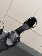 Women's black leather heeled sandal held by hand, wide buckle strap at side