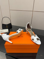 Hermes white leather heeled sandals with cutout strap, shown on orange gift box