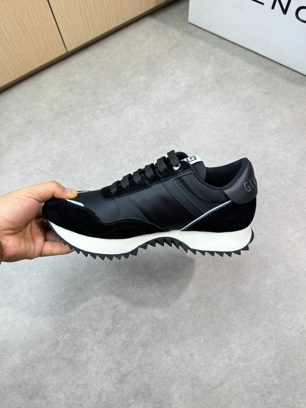 Givenchy black lace-up sneakers, hand-held side view with white outsole contrast