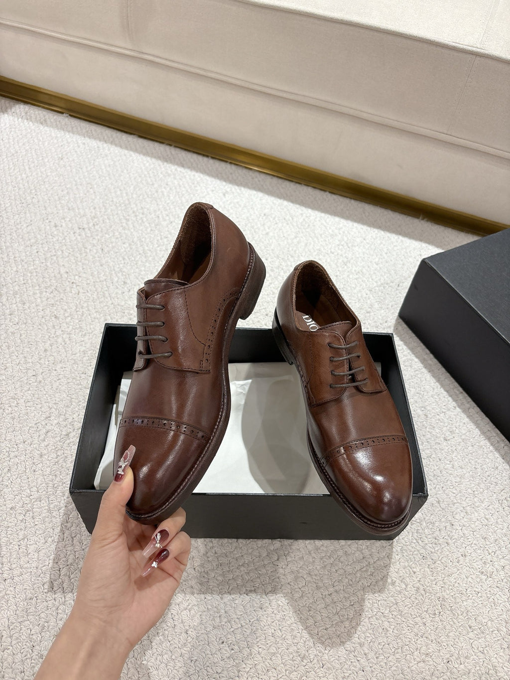Brown leather lace-up dress shoes held by hand above black box