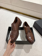 Brown leather lace-up dress shoes held by hand above black box