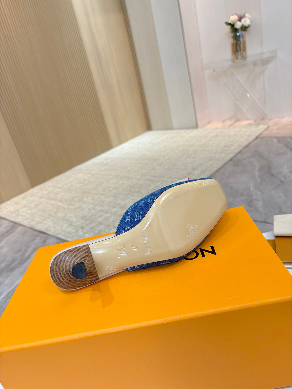 Women's blue monogram mule shoes showing outsoles on orange box