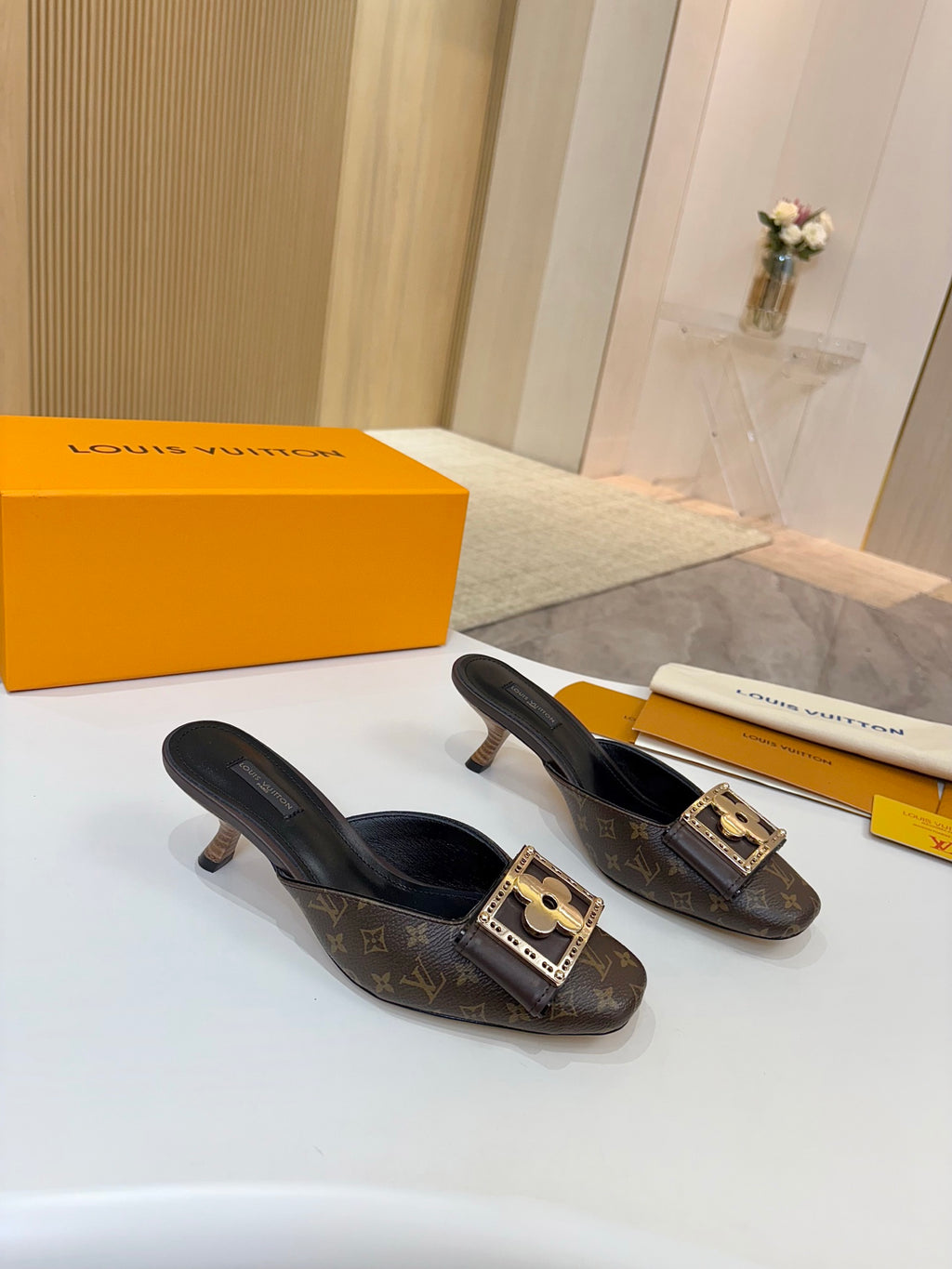Louis Vuitton mule shoes with monogram print, gold buckle accents, in front of box