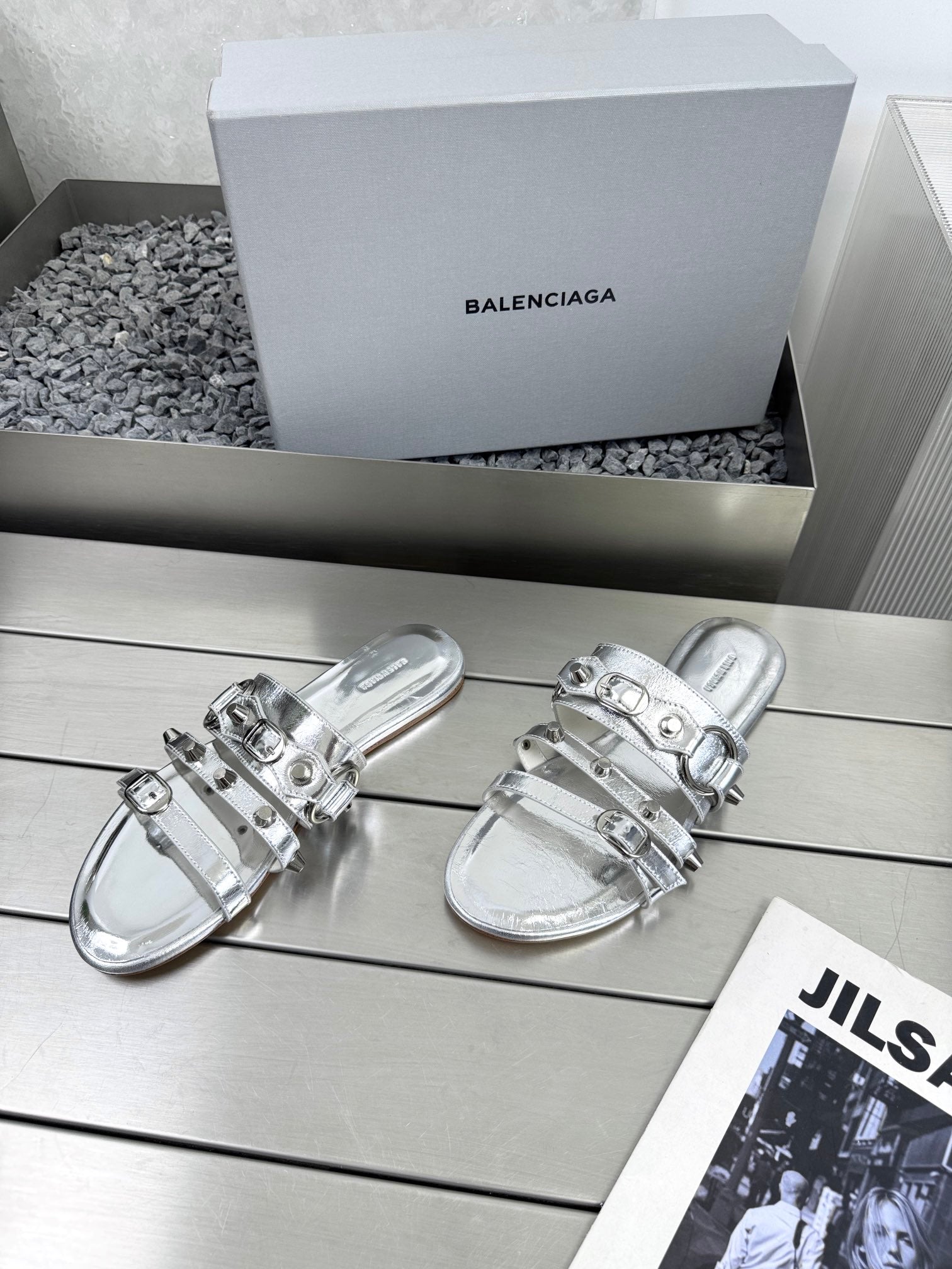 Silver metallic sandals featuring stacked straps and reflective buckle closures